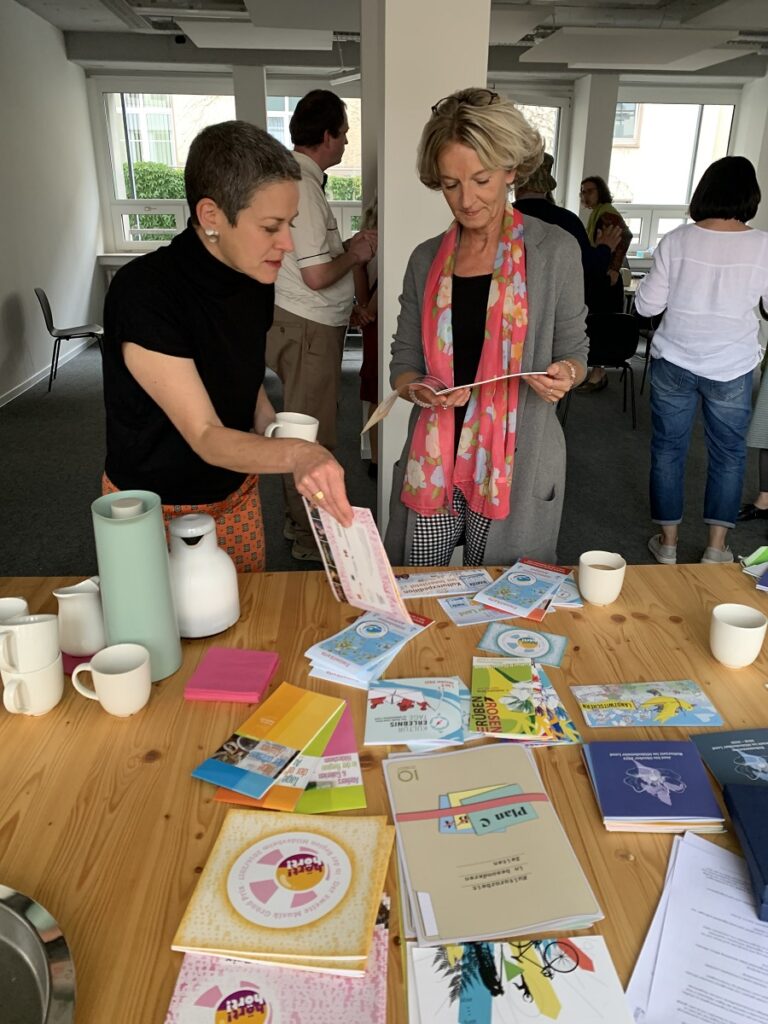 Sabine Zimmermann (Geschäftsführerin, Netzwerk Kultur & Heimat e.V.) und Kathleen Gräf (SB Kulturmanagement, Landratsamt SOK) schauen sich gemeinsam Flyer und Broschüren an.