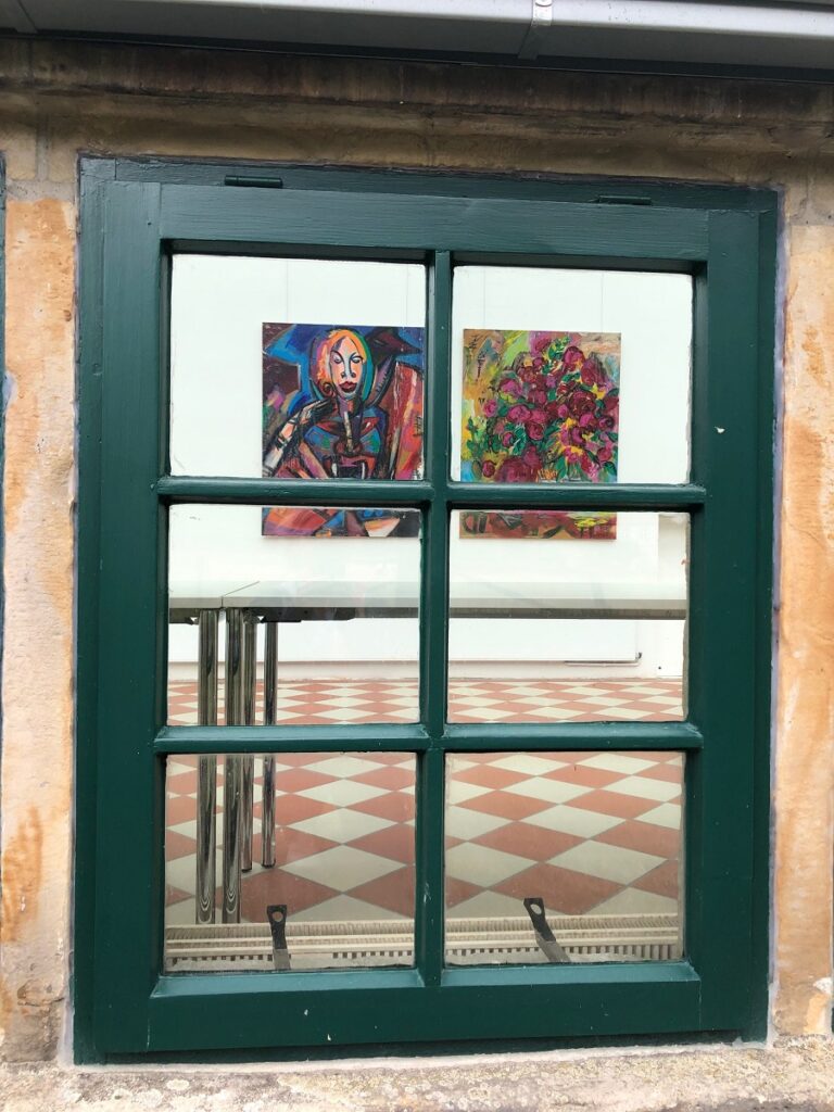 Blick durch ein Fenster auf zwei Gemälde in einem Raum.